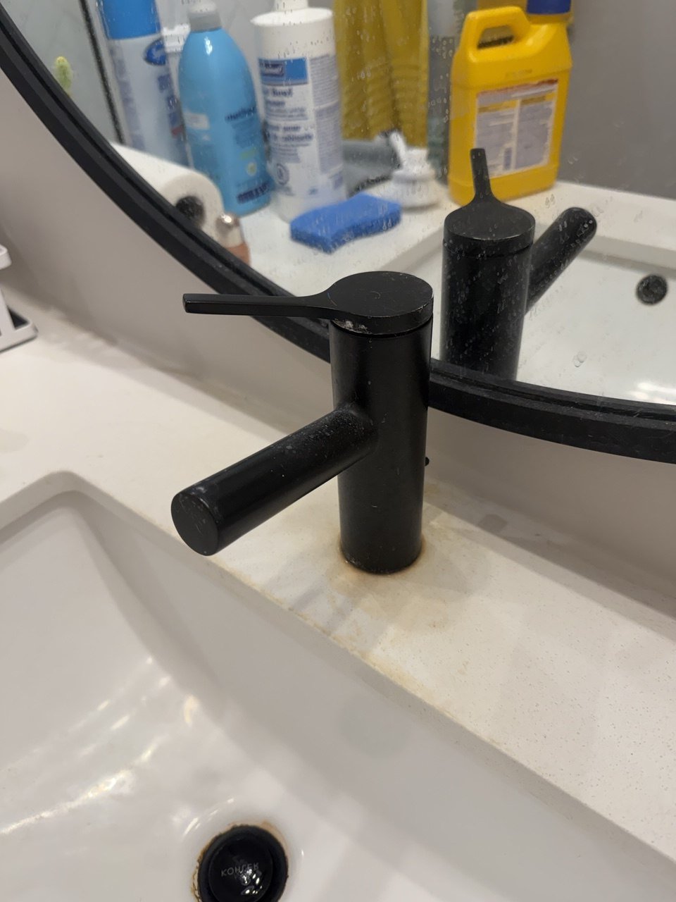 Matte black basin tap before cleaning, with water spots on the spout and dried residue staining the countertop around its base