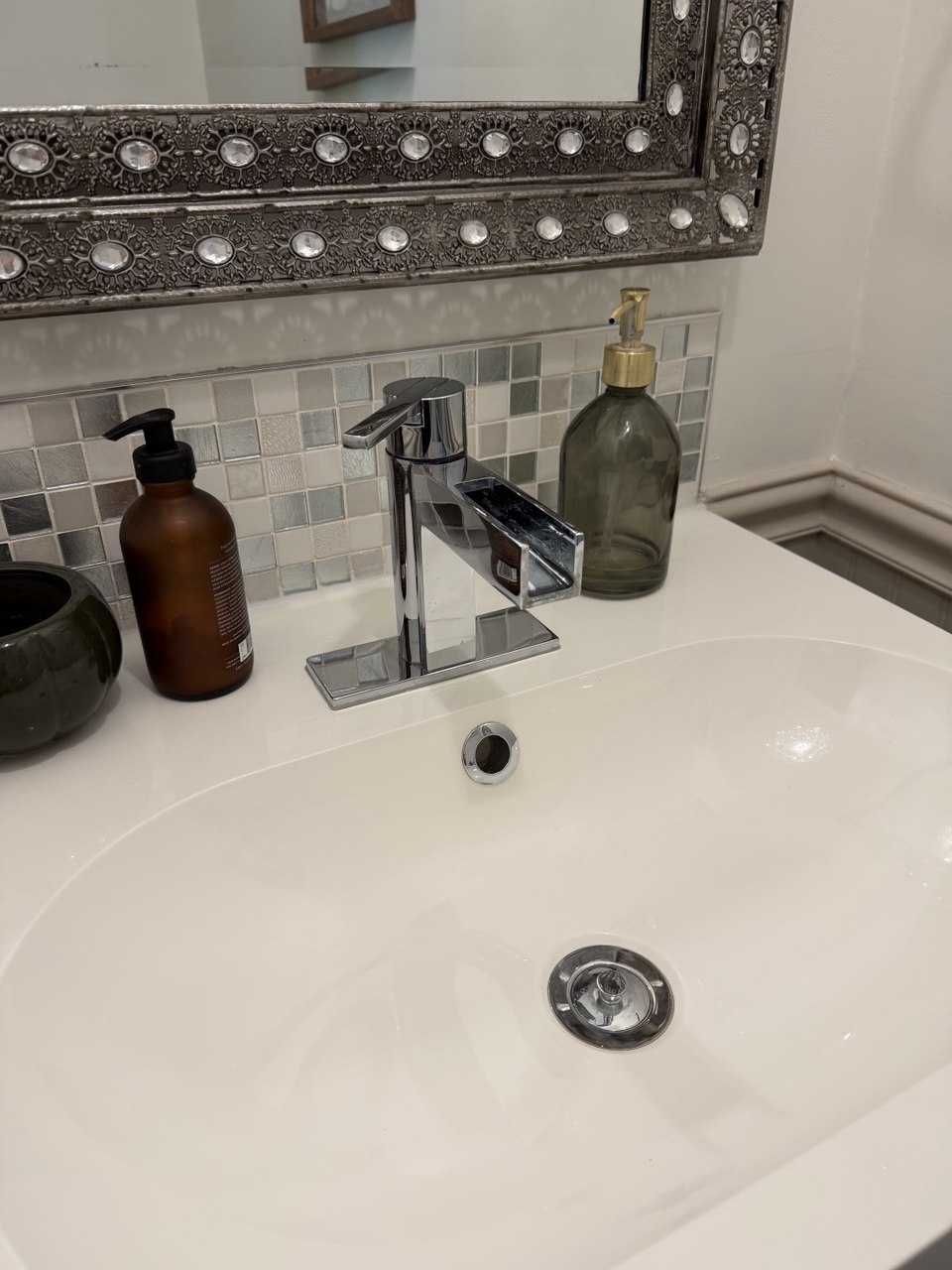 The same vanity after cleaning, with a gleaming chrome tap, bright white basin, and a clear mosaic tile backsplash