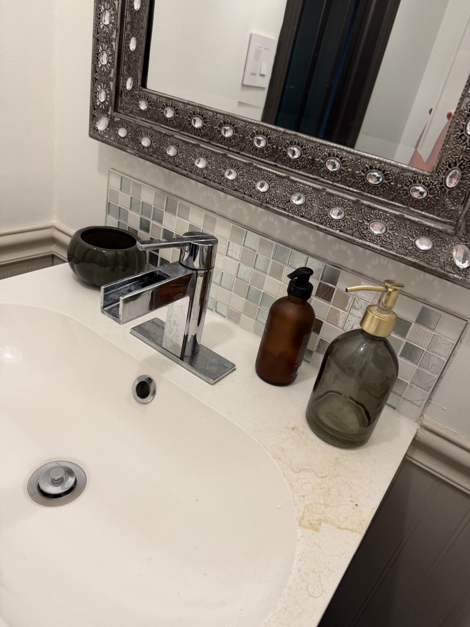 Vanity basin before cleaning, with a dull chrome tap and yellowed marks staining the countertop beside the soap bottles