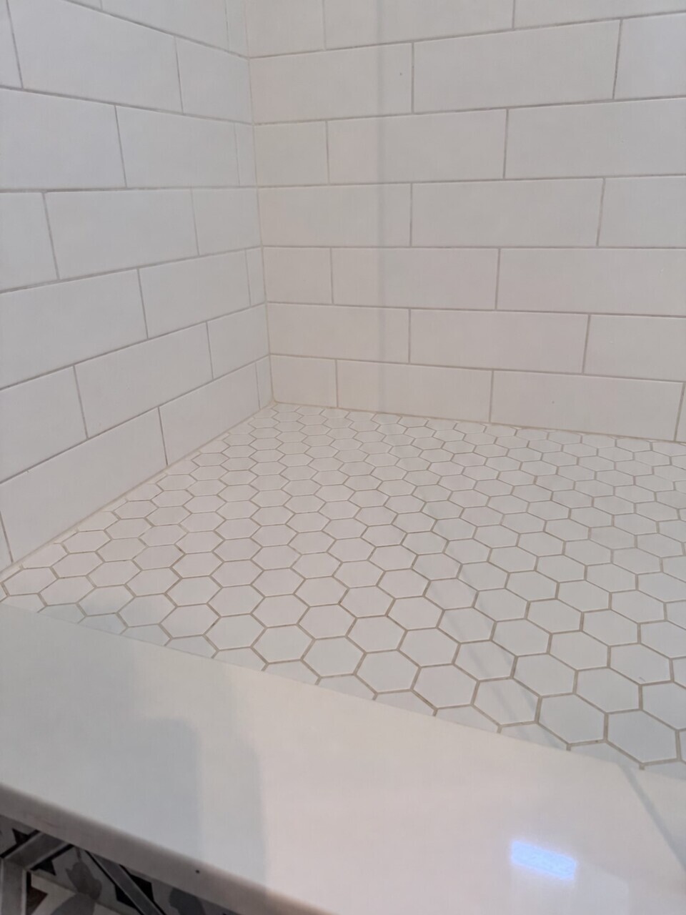 The same shower corner after cleaning, with bright white wall tiles and clean, even grout between the floor tiles