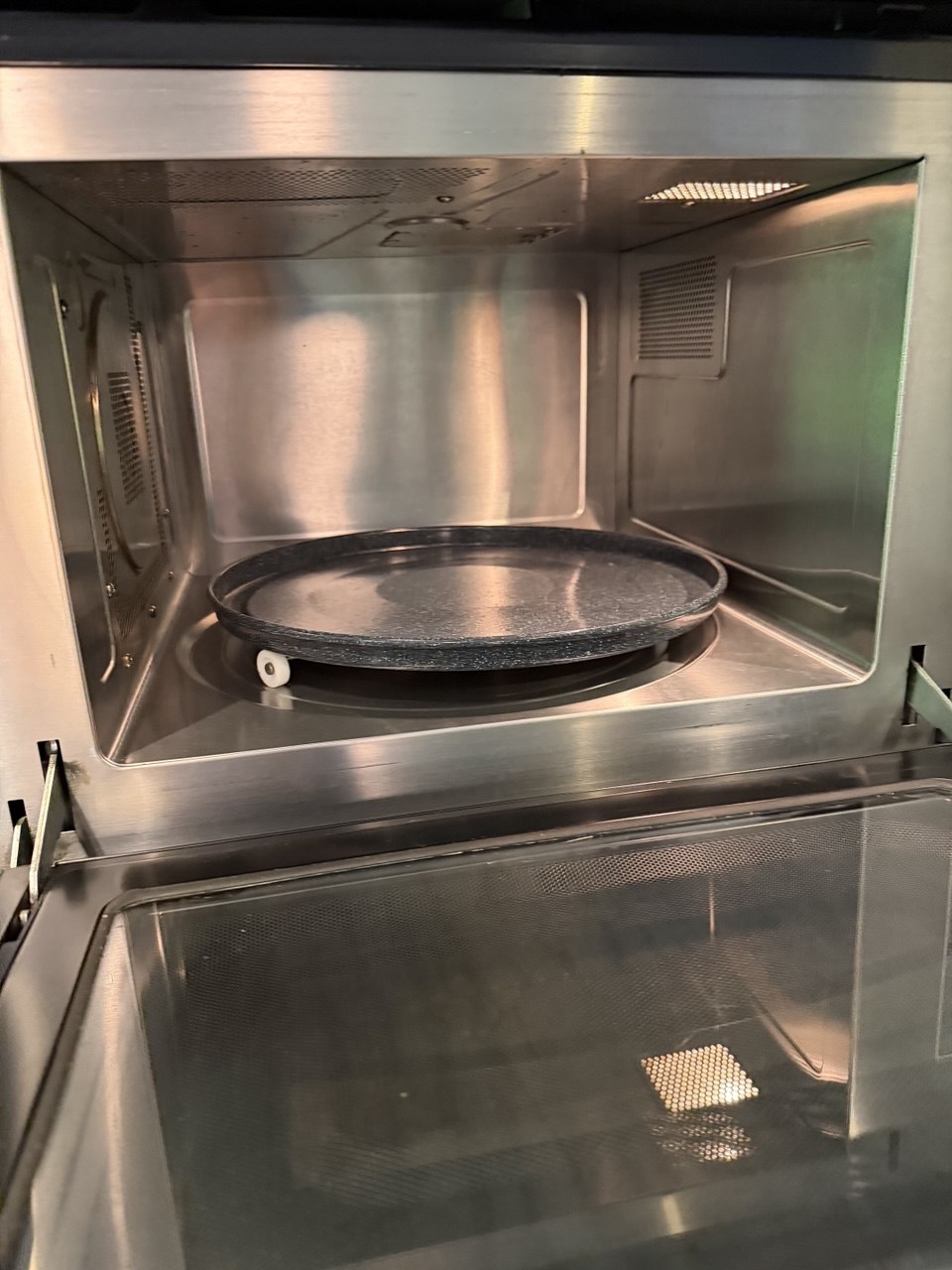 The same microwave oven after cleaning, with spotless stainless steel walls, door, and turntable