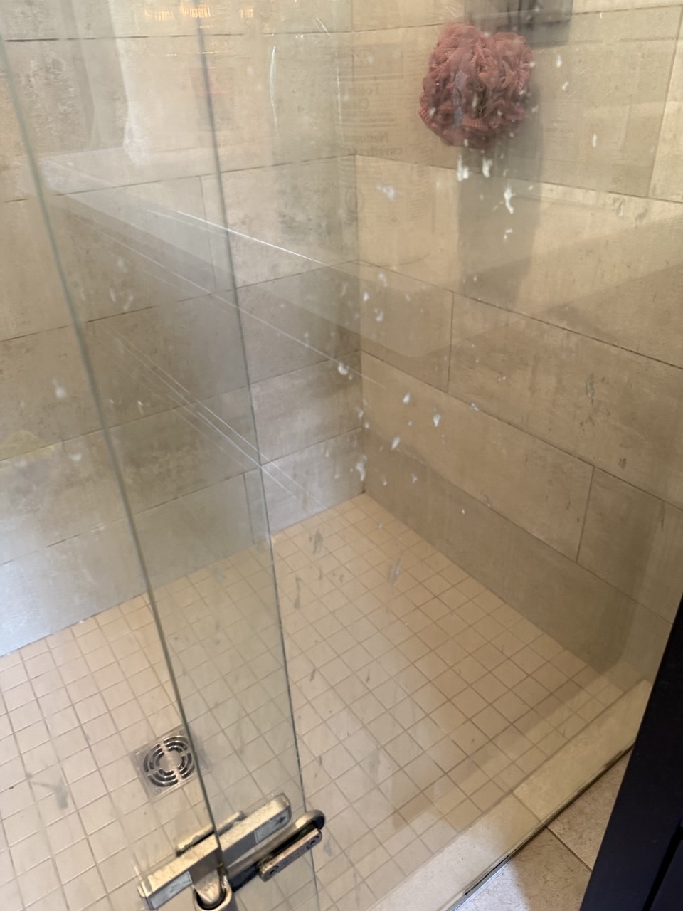 Shower enclosure before cleaning, its glass door clouded with soap splashes and hard water spots